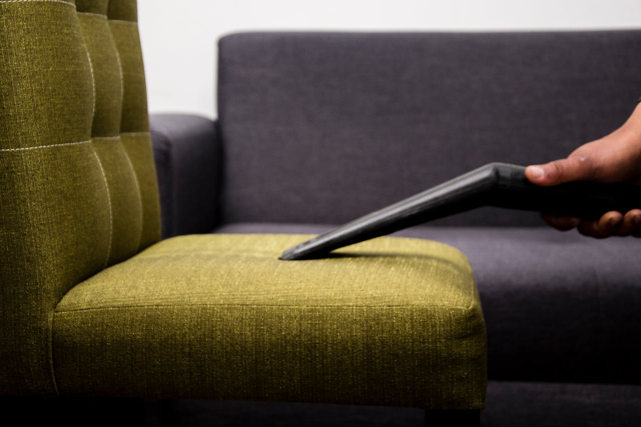 digital Close-up of a person vacuuming a modern sofa chair indoors, highlighting cleaning service.